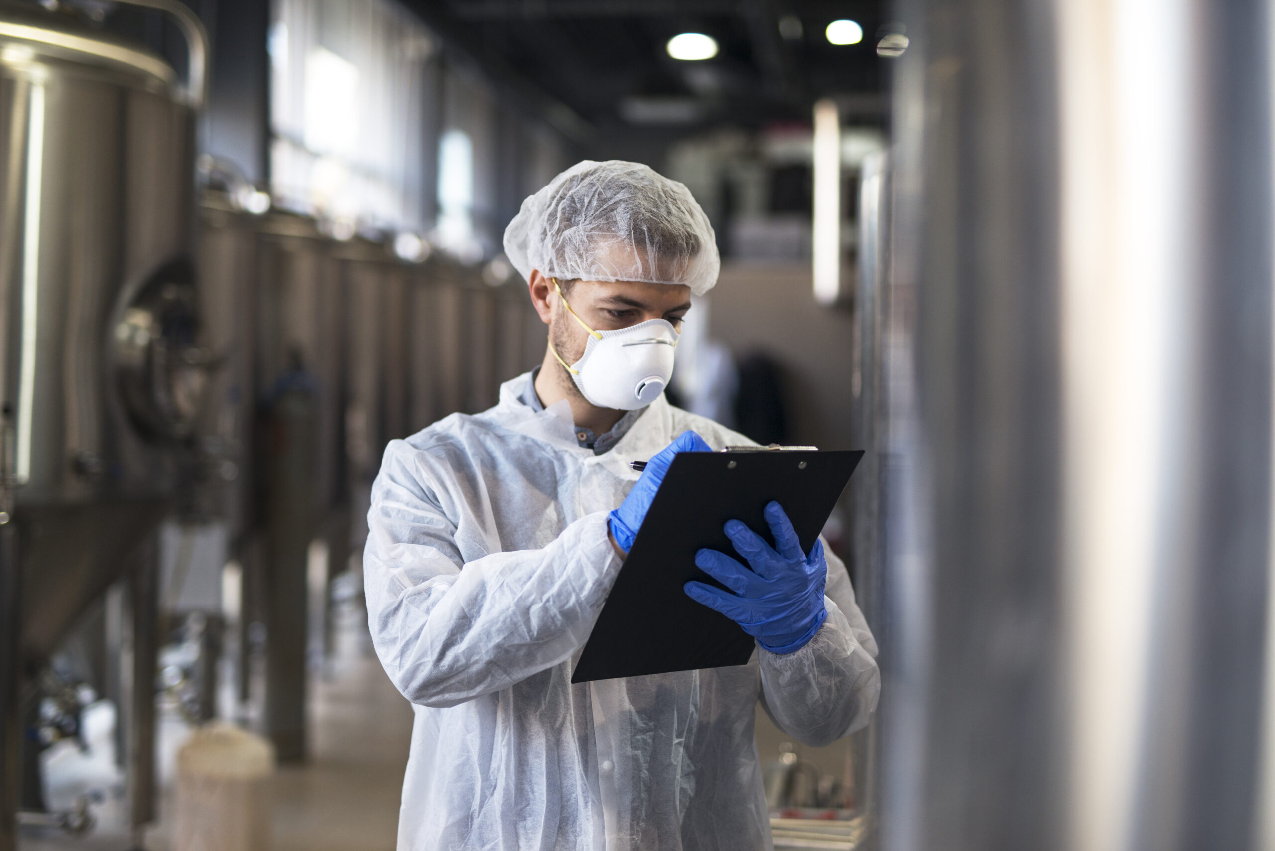 Technologist in white uniform checking quality in industrial production factory.